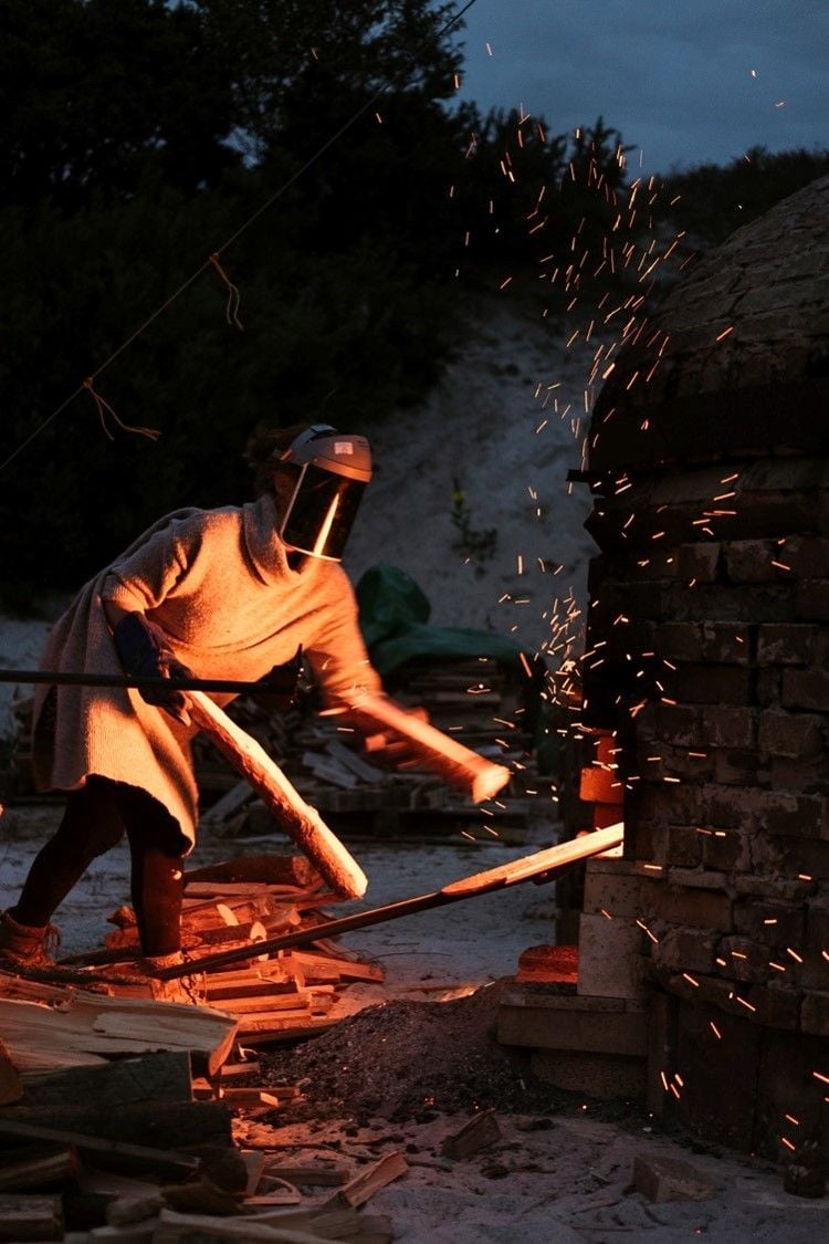 A person in protective clothing feeds fuel to a brick kiln 