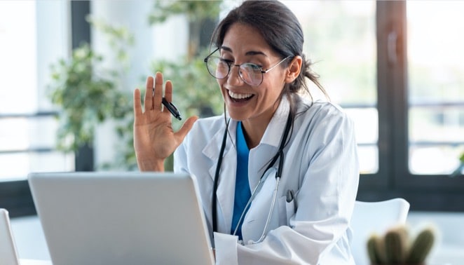 Female doctor waving and talking with colleagues through a video call with a laptop during  consultation
