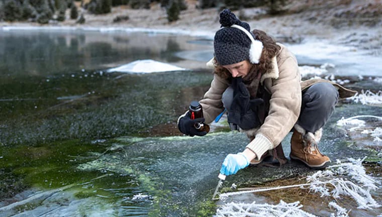 Woman collecting water sample from a frozen lake.