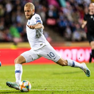 A Finnish football player is about to kick the ball as an Italian player runs towards him.