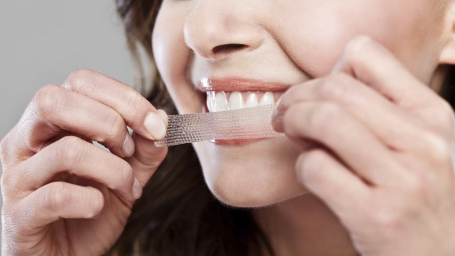 A woman applies a teeth whitening strip to her teeth.