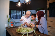 A Muslim sister, brother and mother making food together at a kitchen counter.