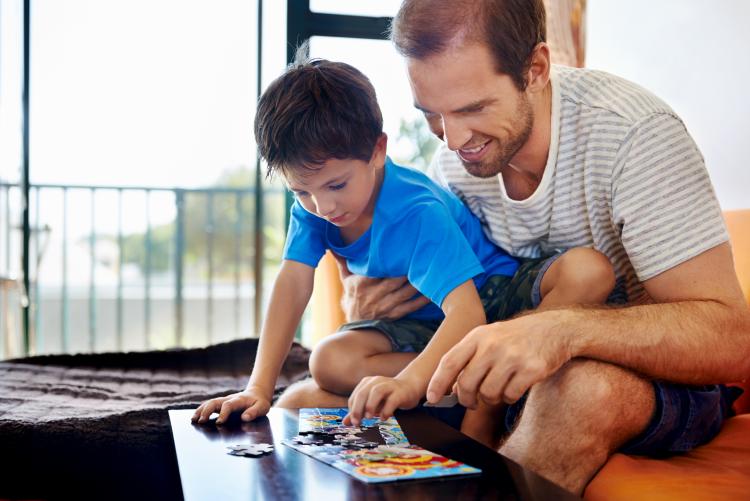 Smiling dad and son building puzzle together.