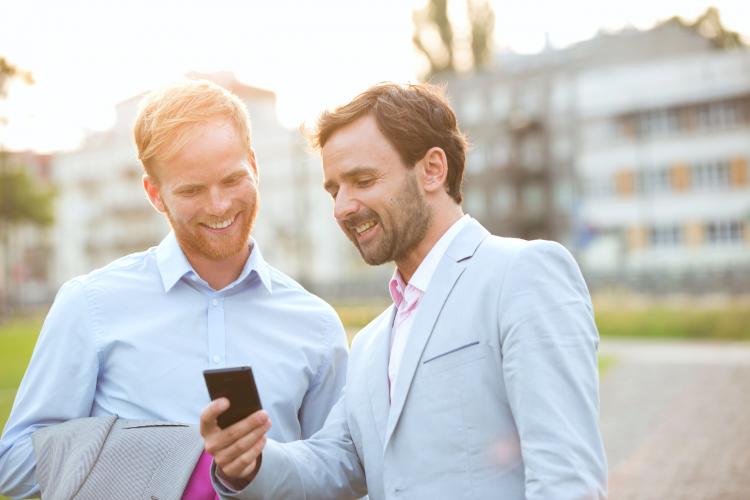 Happy businessmen looking at mobile phone in city.