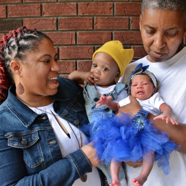 Two people hold their infants together on the front step of their home. 