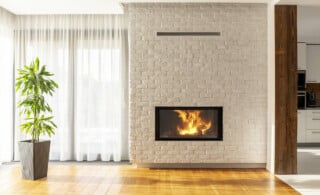 Fireplace on brick wall in bright living room interior of house with plant and windows