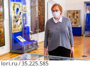 Elderly woman in medical mask examining museum exposition. Стоковое фото, фотограф Яков Филимонов / Фотобанк Лори