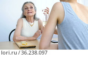 Female portrait of adult daughter and senior mother talking and drinking champagne at home sitting at the table, happy retirement, mothers day concepts, alcohol addiction. Стоковое видео, видеограф Ольга Балынская / Фотобанк Лори