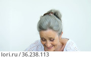 Beautiful old grandmother with grey hair and face with wrinkles is looking at the camera with smile on white background, mothers day, happy retirement. Стоковое видео, видеограф Ольга Балынская / Фотобанк Лори