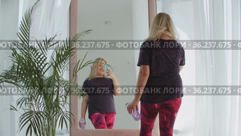 Blonde confident overweight woman walks to a mirror and taking a picture of herself on the phone