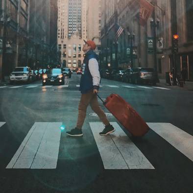 Man walking across the cross walk with a suitcase.