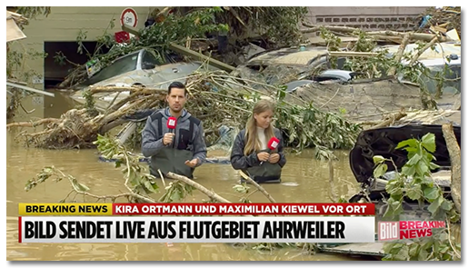 Screenshot aus einem BILD-Video: Zwei BILD-Reporter stehen bis zur Hüfte im Hochwasser, umgeben von weggeschwemmten Autos, Bäumen und Schutt