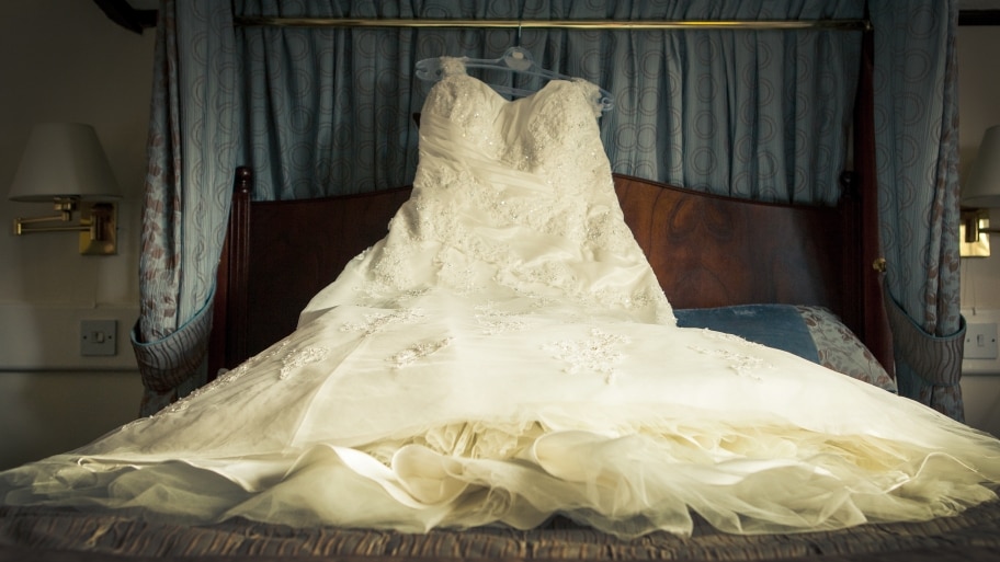 wedding dress on hanger lying across bed