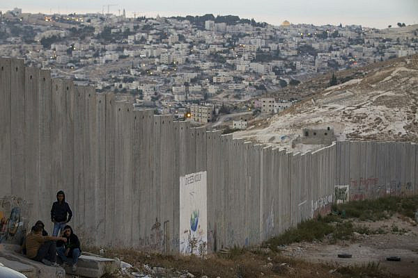 Young Palestinian men sit by a section of the separation wall in the West Bank city of Abu-Dis, September 29, 2014. (Miriam Alster/Flash90)