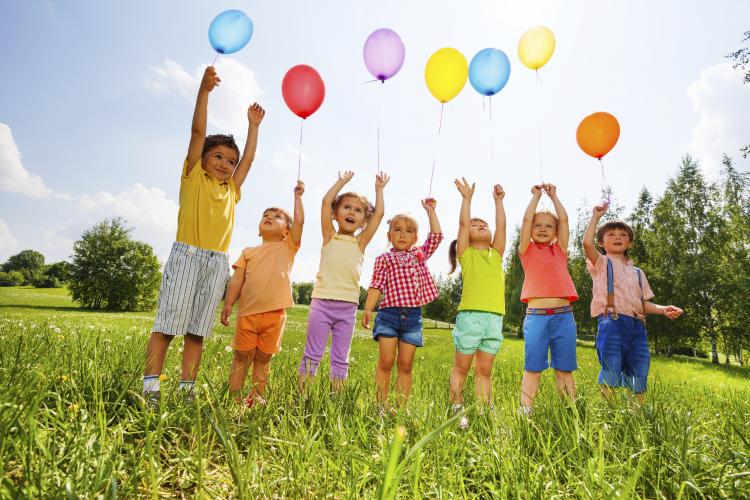 Happy kids with balloons and arms up in the sky.