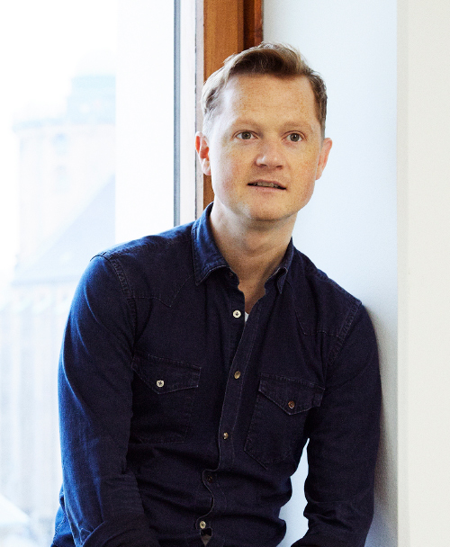 A photograph of Peter Mühlmann – founder and CEO of Trustpilot – sitting in front of a window.