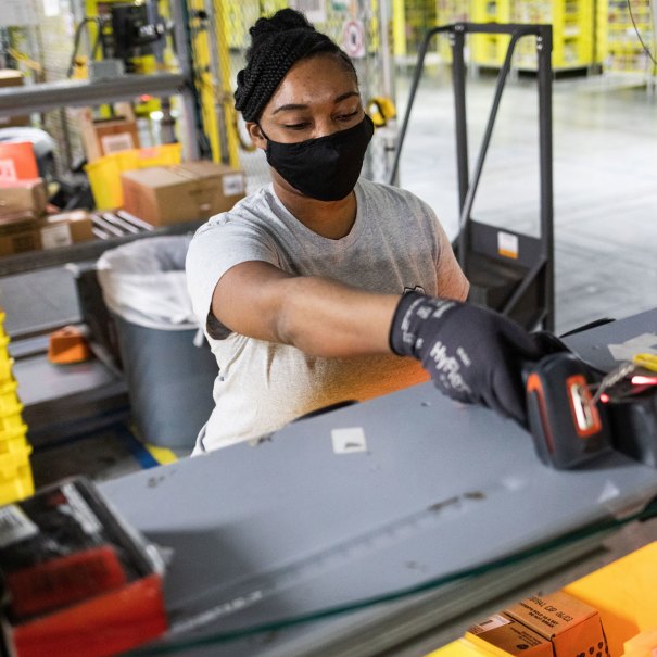 A woman wearing a face mask operates a scanning device inside an Amazon fulfillment center.