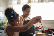 Young girl cooking with her mother.