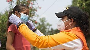 World Vision staff helps child put on a mask for COVID-19