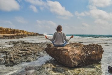 This shows a woman meditating on a rock at a beach