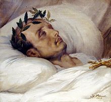 Gold-framed portrait painting of a gaunt middle-aged man with receding hair and laurel wreath, lying eyes-closed on white pillow with a white blanket covering to his neck and a gold Jesus cross resting on his chest