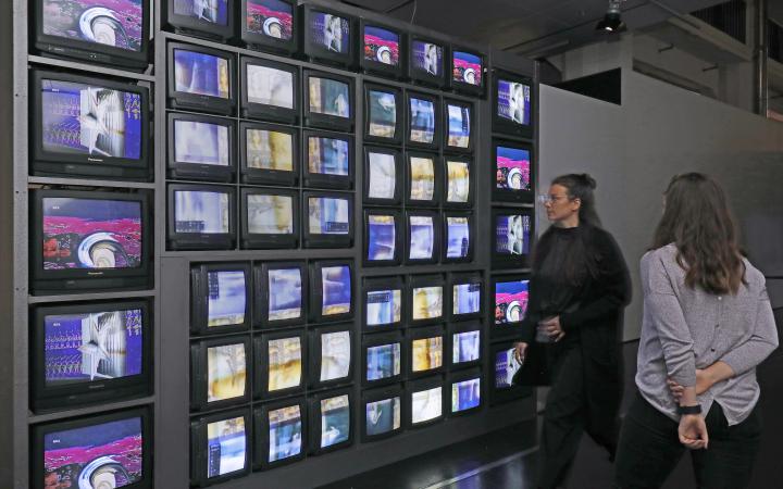 Besucherinnen vor einer Installation aus 52 Monitoren, die eine bunte Bildchoreografie zeigen. 