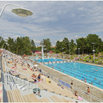 Visitors relax in a seating area overlooking an outdoor swimming pool with trees in the background.