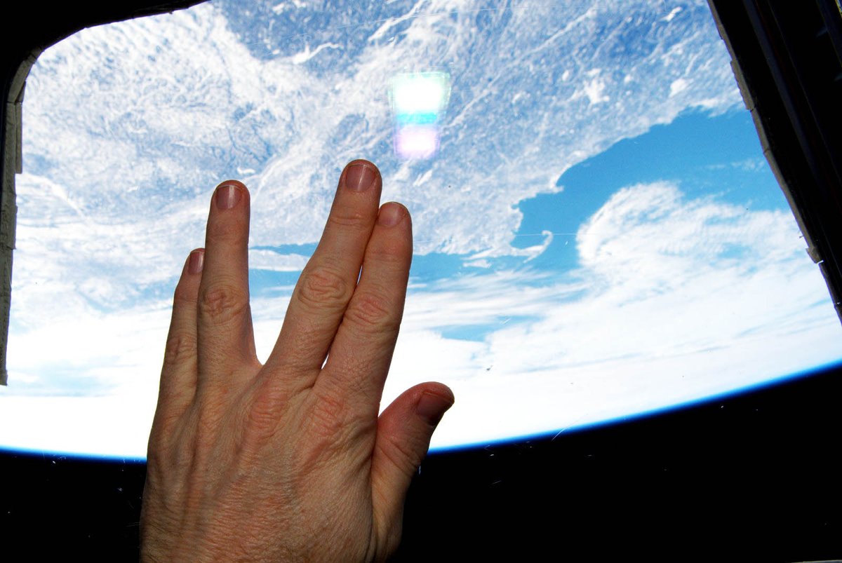 Astronaut's hand making Vulcan salute in cupola of International Space Station, with Earth visible below