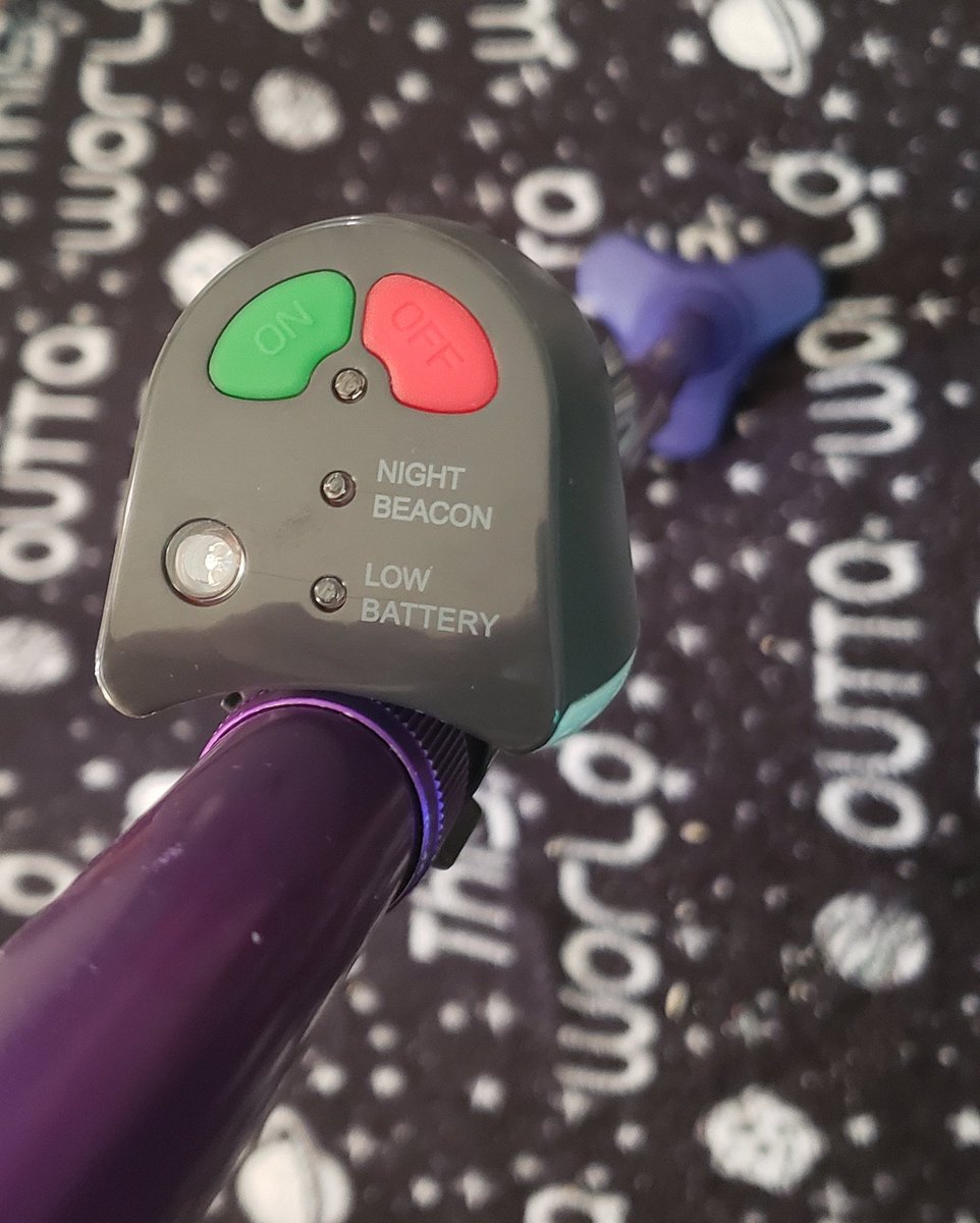 The top of the PathLight, attached to a purple cane. There is a green on button, a red off button, and 2 LEDs labeled Night Beacon and Low Battery respectively.