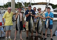 Photo of six men, four of whom are holding up tuna