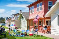 People sitting in the grass outside a colorful row of houses.