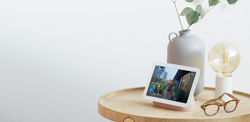 Nest Hub (2nd gen) is on a wooden table inside a home. On the display, a delivery person is at the front door holding a package.