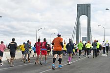 Three runners in a race down a street where onlookers are cheering behind barriers.