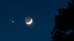 Crescent Moon with dark blue sky in the background. The unlit part of the Moon has a dim glow. Bright star shines to the left of the Moon.