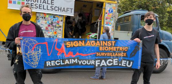 Zwei Menschen halten ein Reclaim Your Face Banner hoch und stehen vor einem Lautsprecherwagen bei der unteilbar-Demo in Berlin 2021.