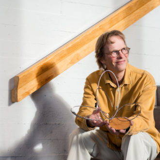 A man sits on a stairway holding a sculpture made of metal rings and wood.