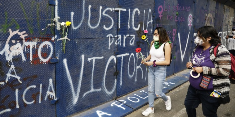 Young women bring flowers to the perimeter wall of the Quintana Roo state offices sprayed with graffiti that reads in Spanish "Justice for Victoria," during a protest in Mexico City on March. 29, 2021.