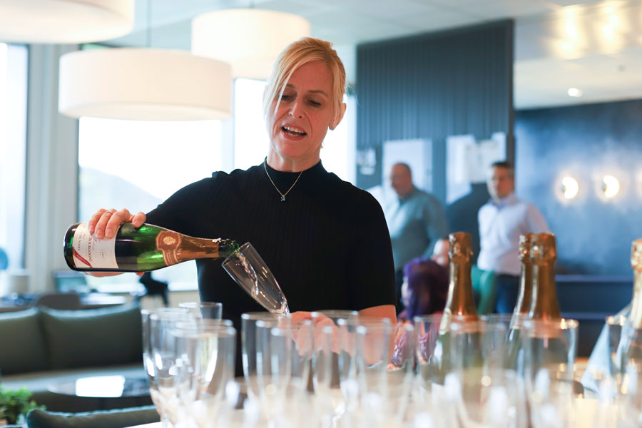 A blonde woman pouring sparkling wine