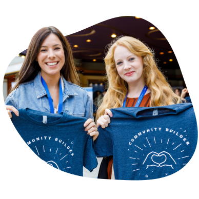 Two women holding up "community builder" t-shirts