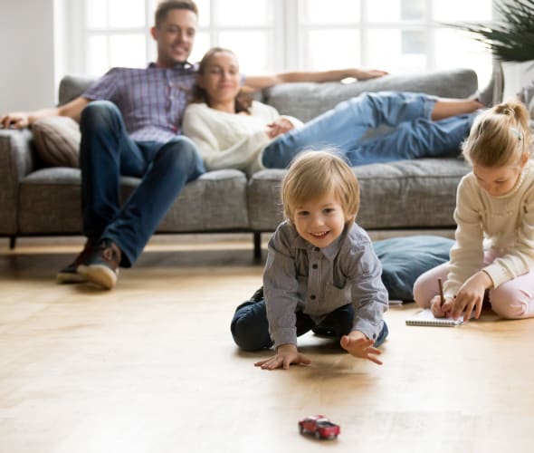 Little boy reaching for a toy car on the floor while his parents and sister watch