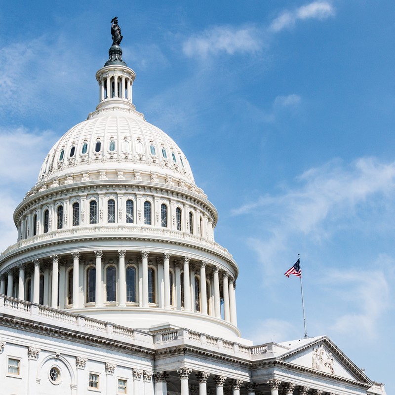 An image of the United States Capitol Building, home of Congress. There is a blue sky behind the building and an American flag flying on its roof.