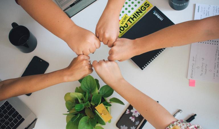 Five closed fists touching over a table