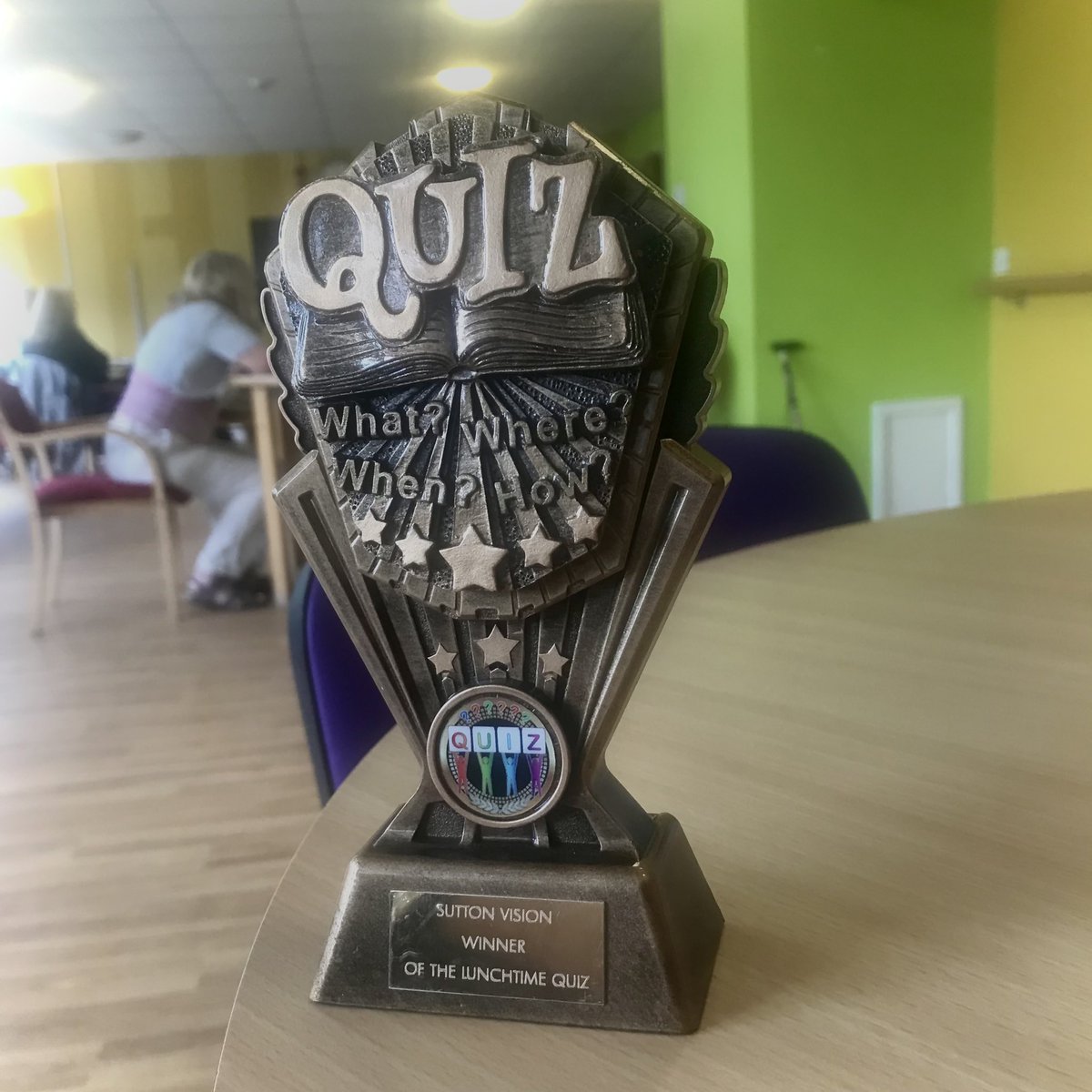 A trophy is on the table with the word Quiz, what? When? Where? How? On the top and Sutton Vision winner of the lunchtime quiz on the base.