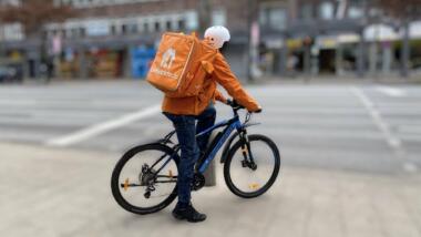 Ein Lieferando-Fahrer auf einem Rad vor einer verschwpommen fotografierten Straße