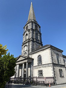 A Large Church spire can be seen above and behind a theatre and a deciduous tree with leaves shed.