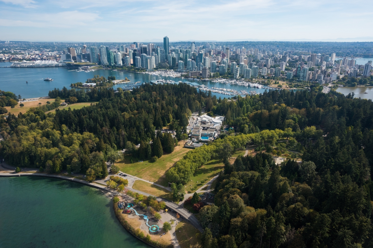 Tall buildings in a city near water with a large, green tree-filled park in the foreground