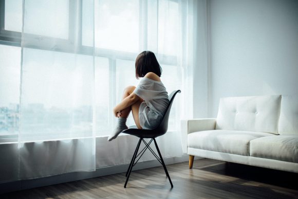 Photo of a young woman staring out the window. Her body language suggests isolation and a feeling of being unsafe.