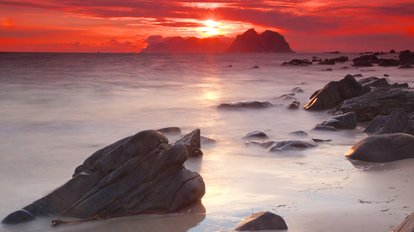 Felsige Küste und Meer mit tief stehender Sonne und rot angestrahlten Wolken.