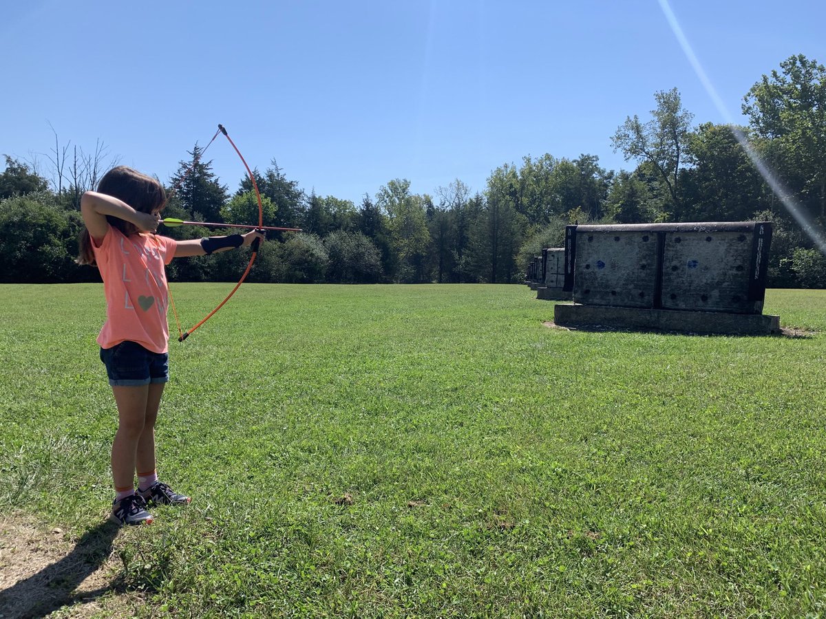 A child drawing a bow to send an arrow to an archery target