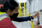 A woman wearing a mask and safety vest pulls down on a lever.